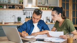 casal em casa a preencher documentos com um portatil aberto